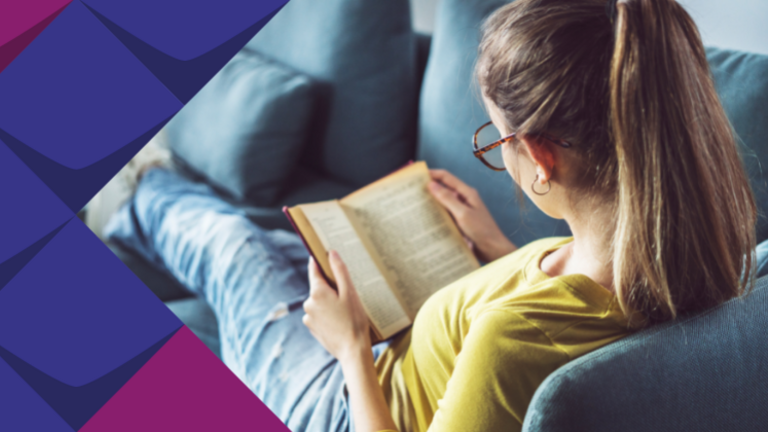 Foto einer Frau mit Brille, die ein Buch liest und auf dem Sofa liegt