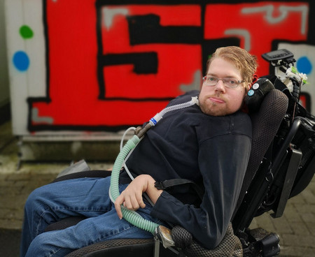 Tim sitzt in einem Rollstuhl vor eine Wand mit Graffiti