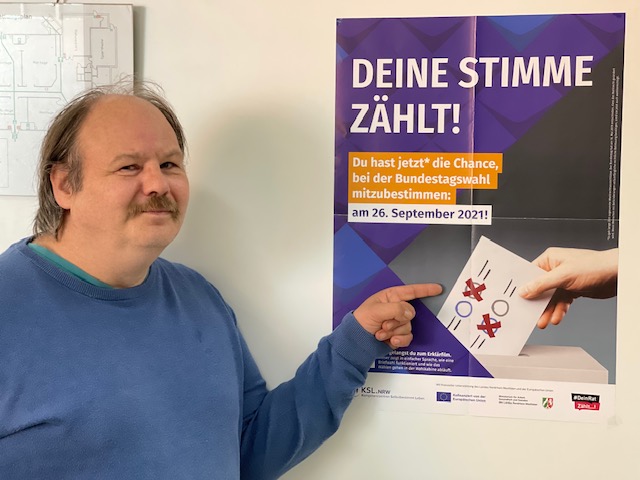 Foto von Gerd Ziegler. Er zeigt auf das Plakat der KSL NRW