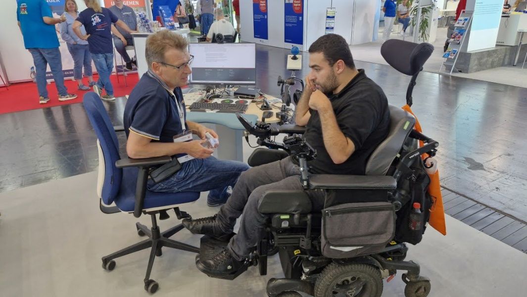 Zwei Rollstuhlfahrer auf der Messe vor einem Büroarbeitsplatz
