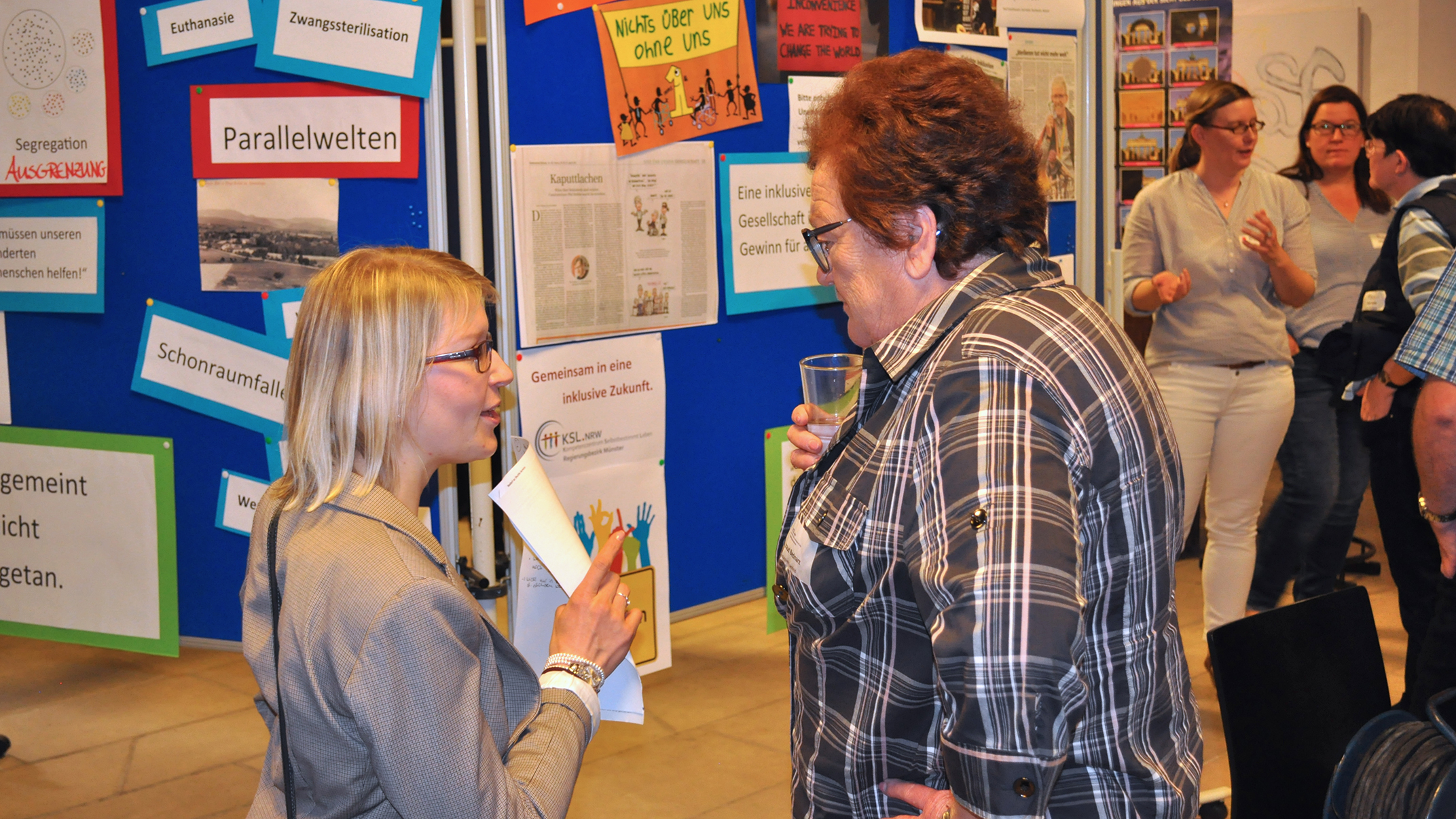 Eindruck von der Veranstaltung "Mehr Partizipation wagen!" auf Burg Vischering im Regierungsbezirk Münster. Eindruck von der Veranstaltung. Zwei Frauen unterhalten sich vor einer Pinnwand, auf der Schlagwörter zum Thema Inklusion angebracht sind.