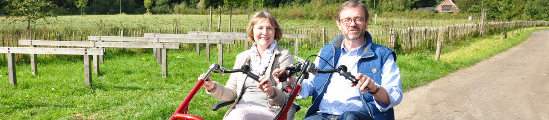 Dreirad-Tandem vor Haus Heidhorn, der NABU-Naturschutzstation Münsterland Ein Dreirad-Tandem wird von einem Mann und einer Frau durch eine ländliche und sonnige Umgebung gefahren