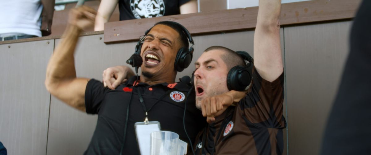 Das Bild zeigt zwei junge Männer auf der TrDer Mann rechts im Bild ist der Schauspieler David Knors. Links ist sein Freund. Sie liegen sich in den Armen und jubeln über ein Tor des FC Sankt Pauli. Foto: Port au Prince