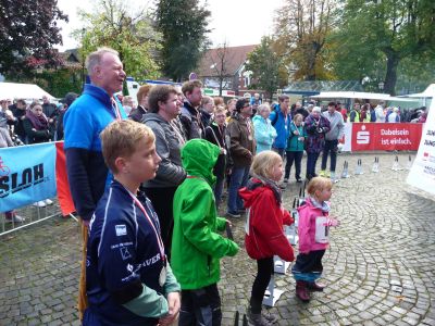 Viele Menschen stehen vor der Bühne und warten im Sonnenschein auf die Siegerehrung.