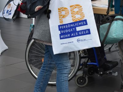 Junge Frau mit einer Stofftasche, auf der das Logo der Persönlichen Budget-Kampagne aufgedruckt ist.