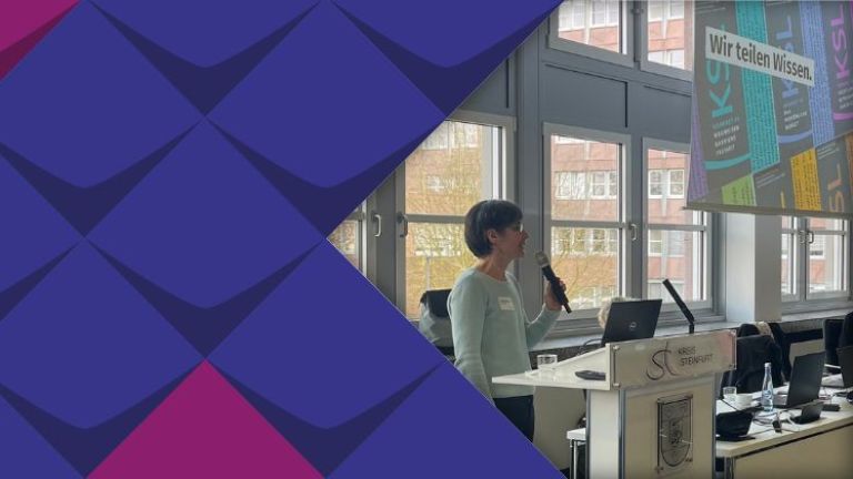 Martina Steinke vom KSL.Münster steht bei einer Veranstaltung am Rednerpult mit einem Mikrofon in der Hand. Im Hintergrund ist eine Präsentation der KSL.NRW auf einer Leinwand zu sehen. Auf der Folie steht "Wir teilen Wissen."